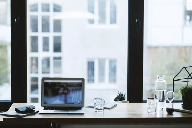 Sleek office desk setup featuring a laptop, glass of water, and open window view. Arbejdspladsvurdering ved hjemmearbejde: Hvad kræver loven?