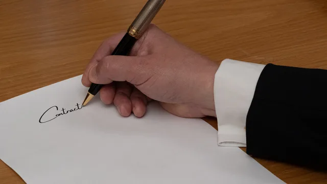 A professional signing a business contract with a fountain pen on a wooden desk. Hvilke krav gælder til en ansættelseskontrakt?