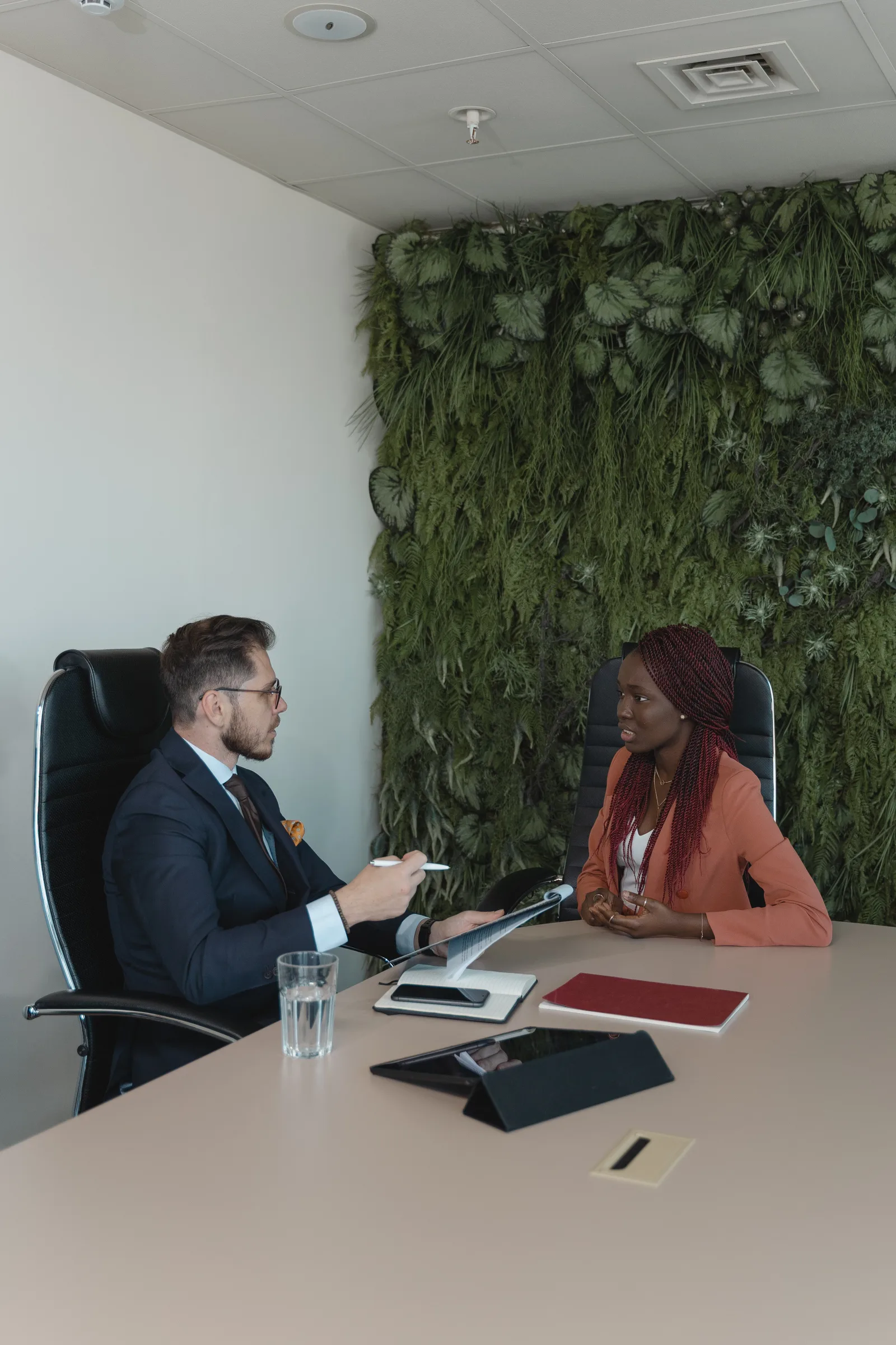 A man and woman engaged in a professional meeting with a green plant wall backdrop.